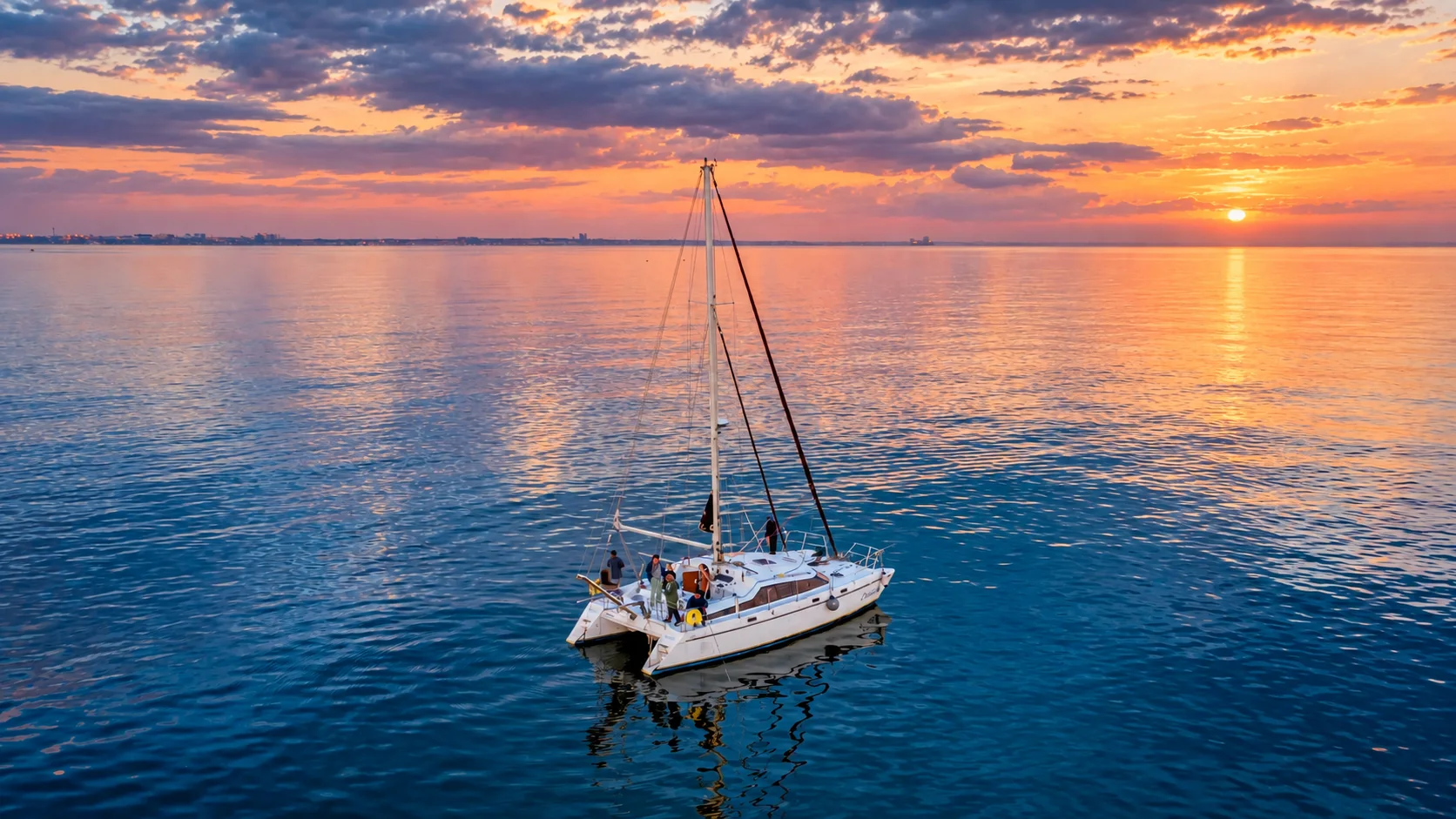 A catamaran sailing across open water at sunset.
