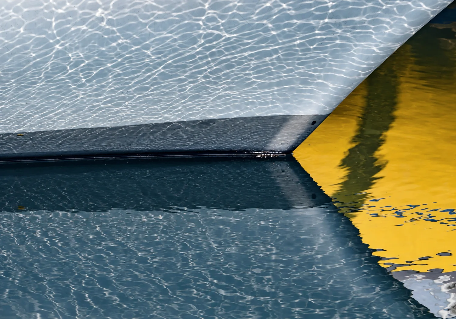The geometry of a yacht hull reflected in still water.