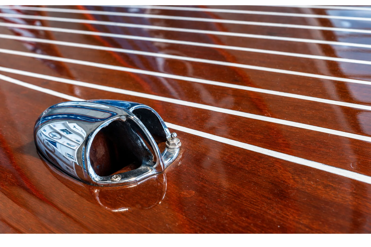 A chrome deck fitting set into a varnished yacht deck.