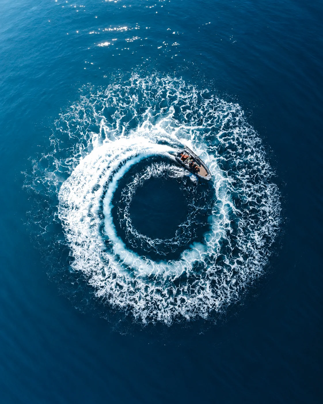 A speedboat tracing a circular wake across blue water.
