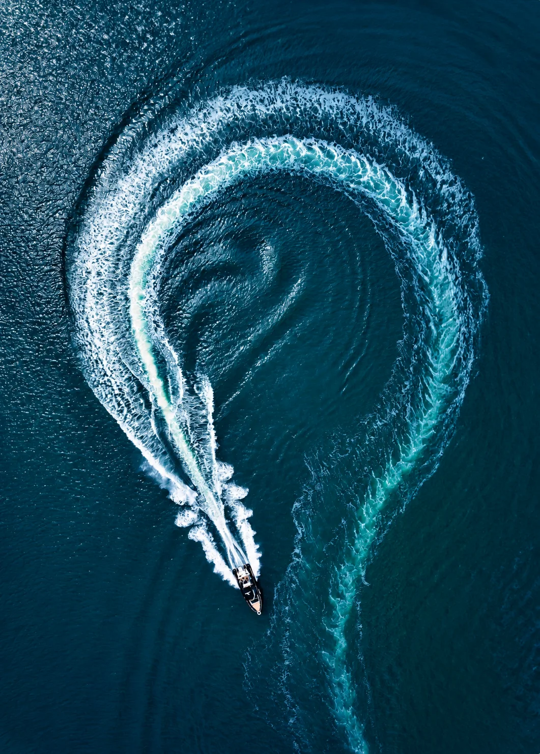 A yacht drawing a circular wake across open water.