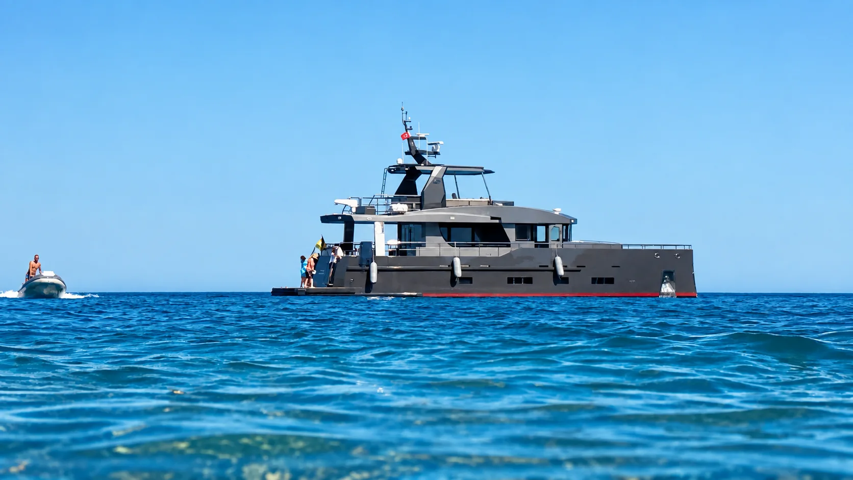 A grey expedition yacht cruising through clear azure water.
