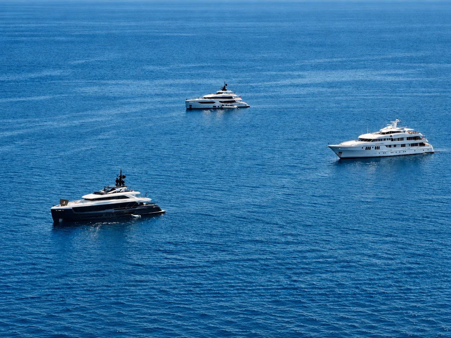 Three different motor yachts spaced across open blue water.
