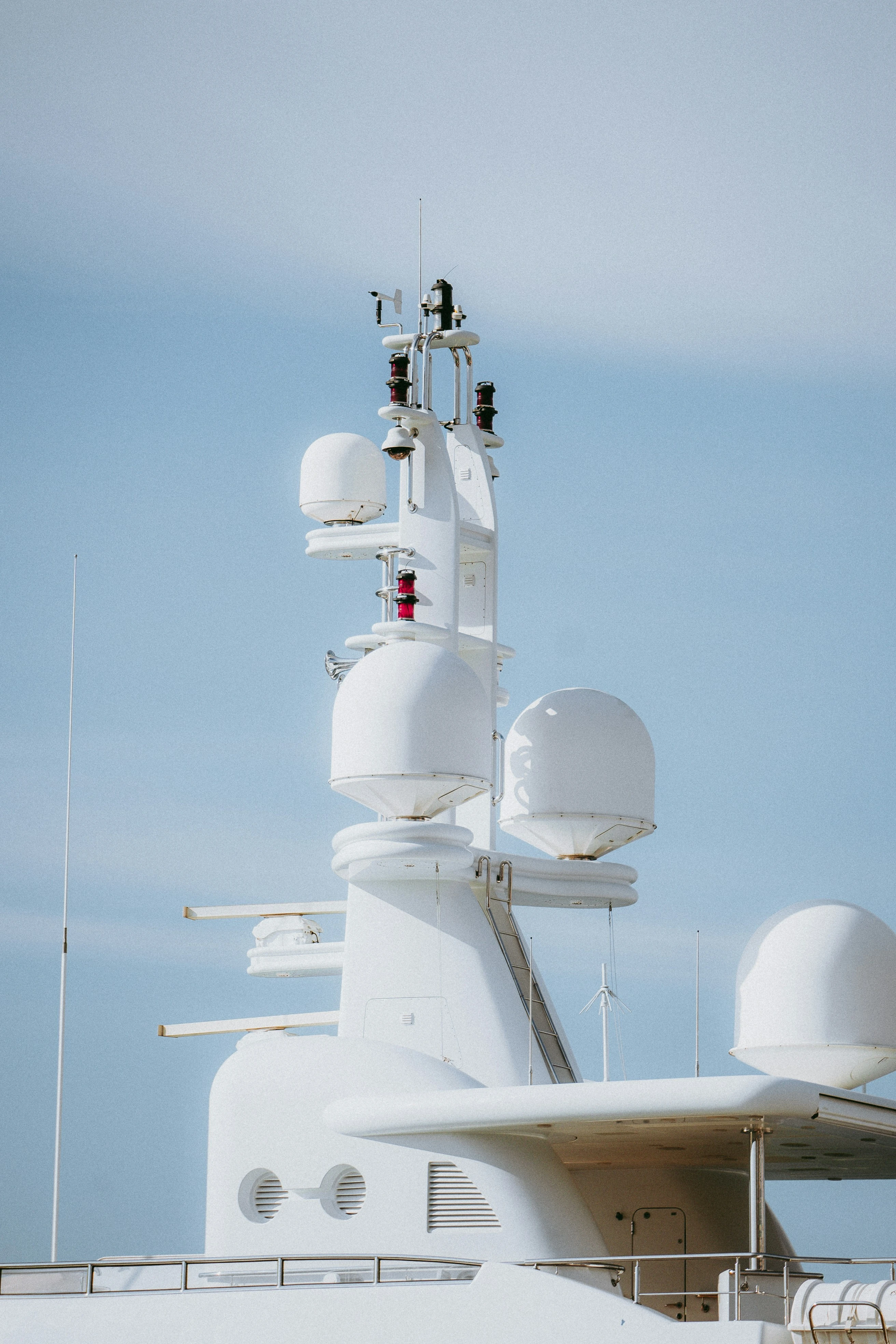 White yacht mast, radar domes and antennas against a pale blue sky