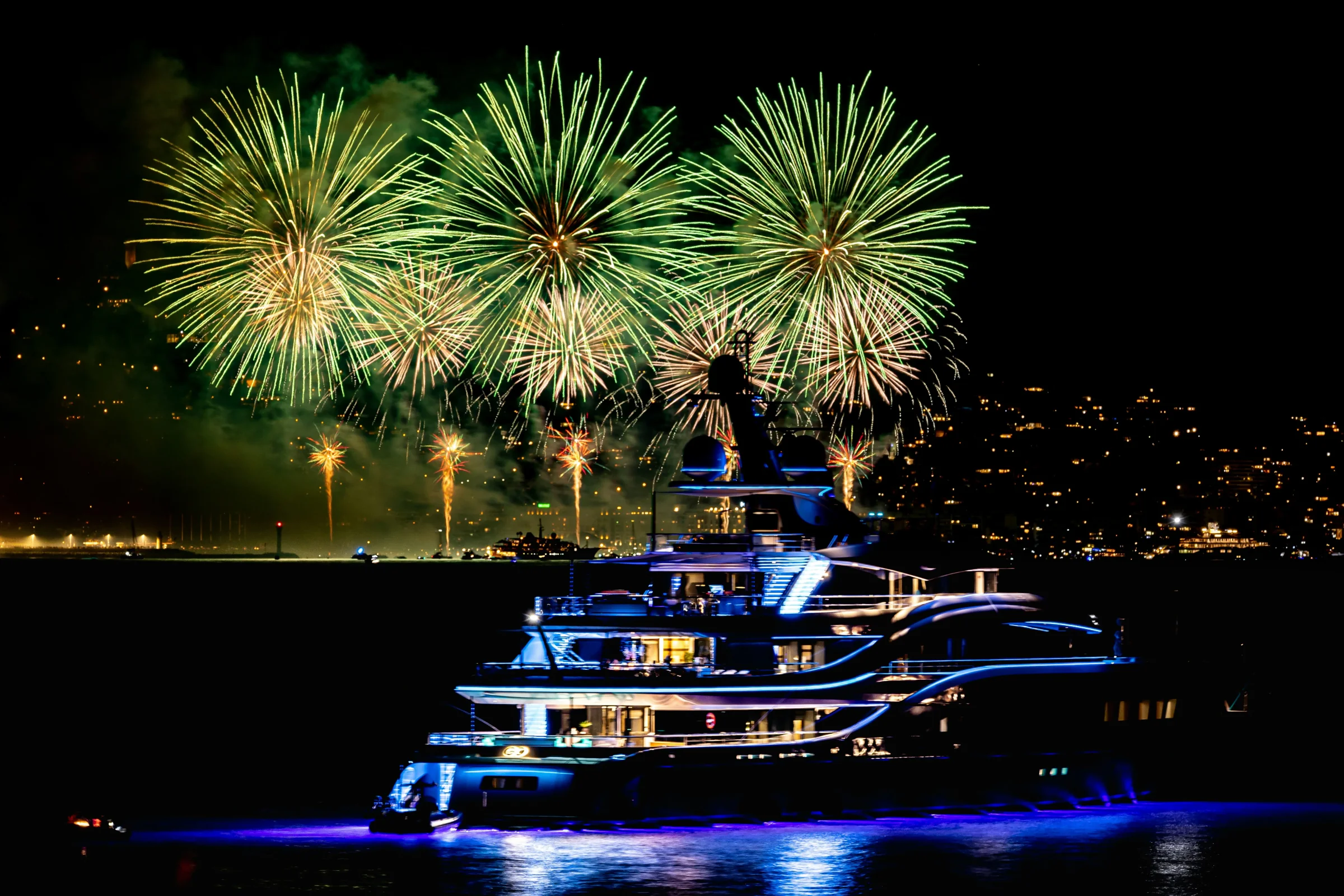 A superyacht on the water beneath green and gold fireworks at night