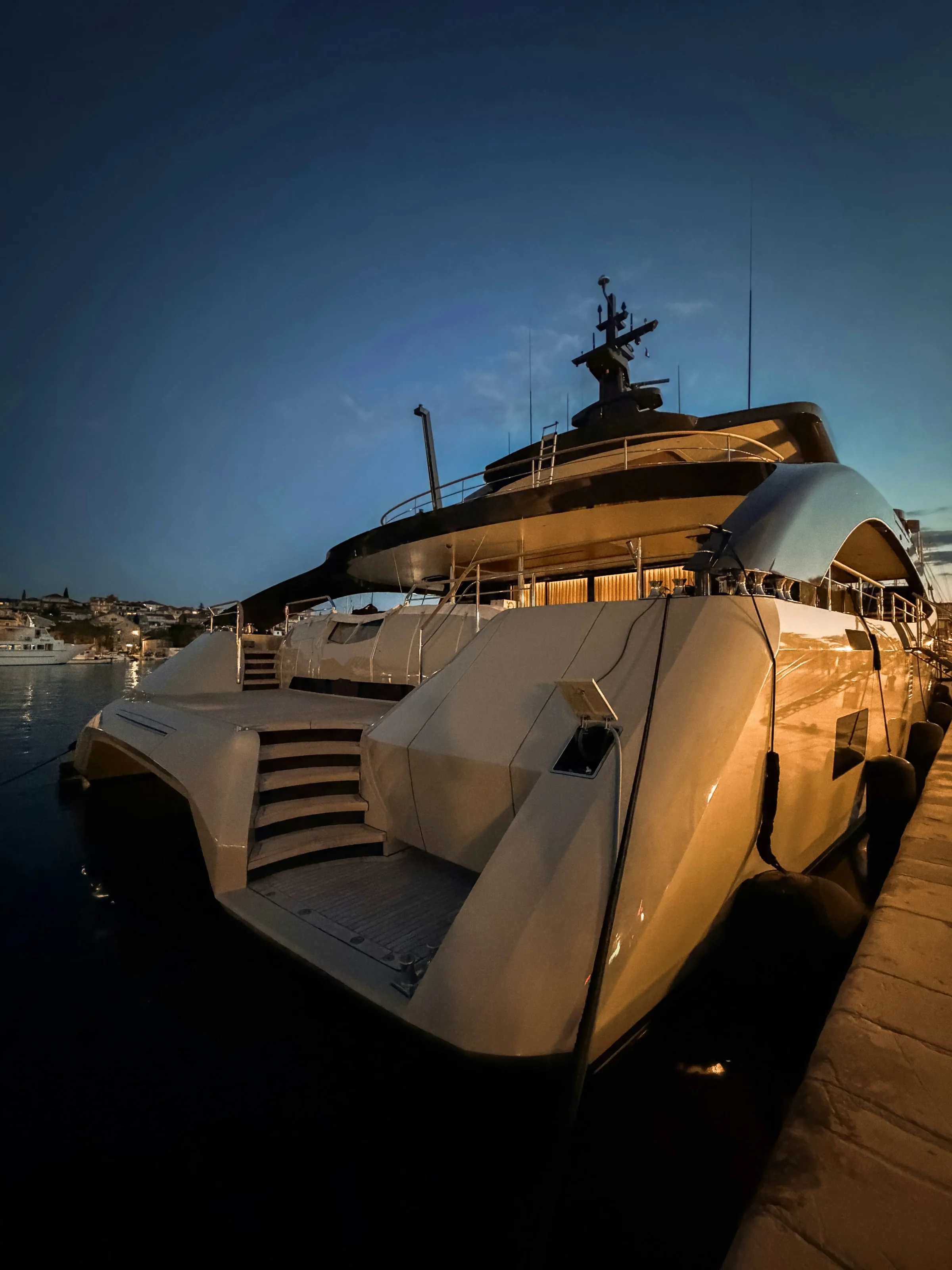 The stern of a motor yacht lit at dusk in a marina