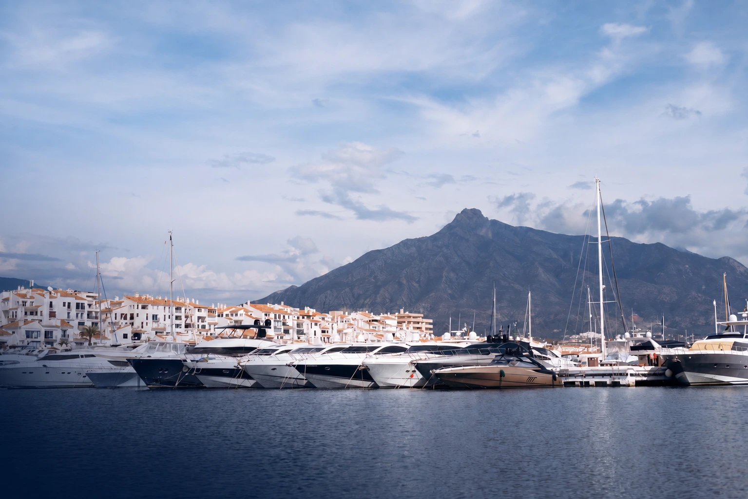 Yachts moored in Puerto Banús with waterfront buildings and mountains behind them